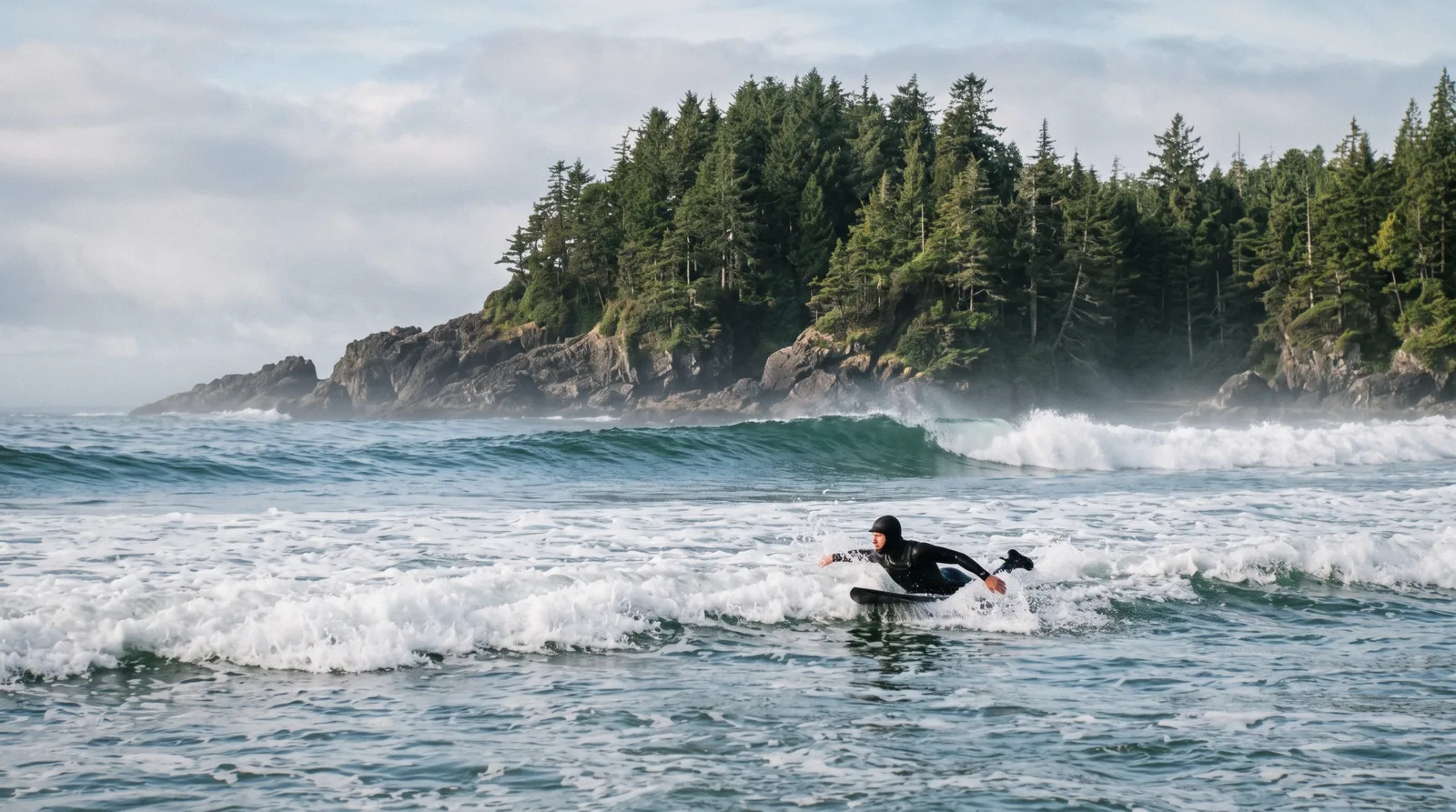 Surfer in a wetsuit walking toward the waves at Cox Bay near Tofino, British Columbia