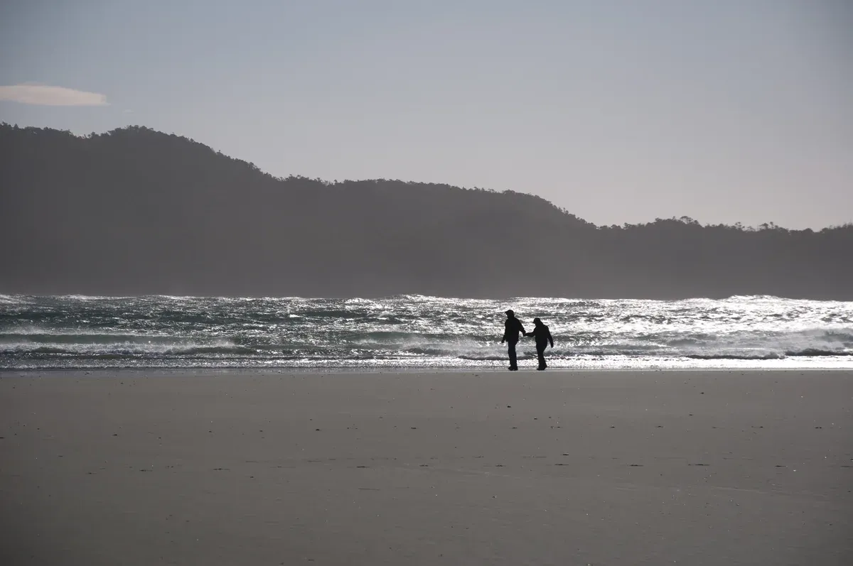 Two people walking the shoreline at Chesterman Beach near Tofino, British Columbia, with surf breaking behind them